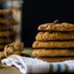 A tempting stack of chocolate chip cookies on a cloth napkin with crumbs around.